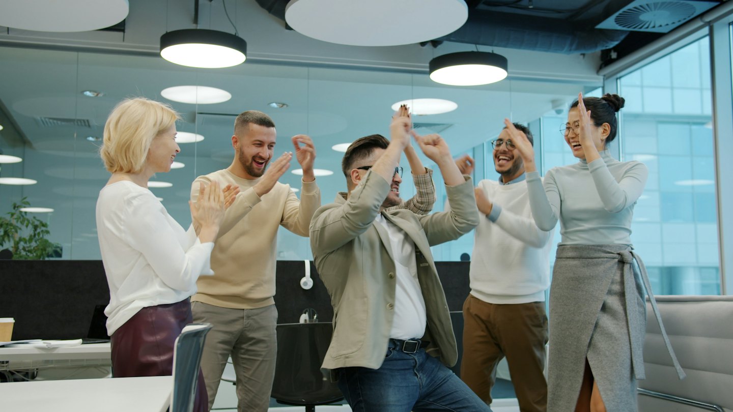 Business team celebrating success and clapping in a bright office.