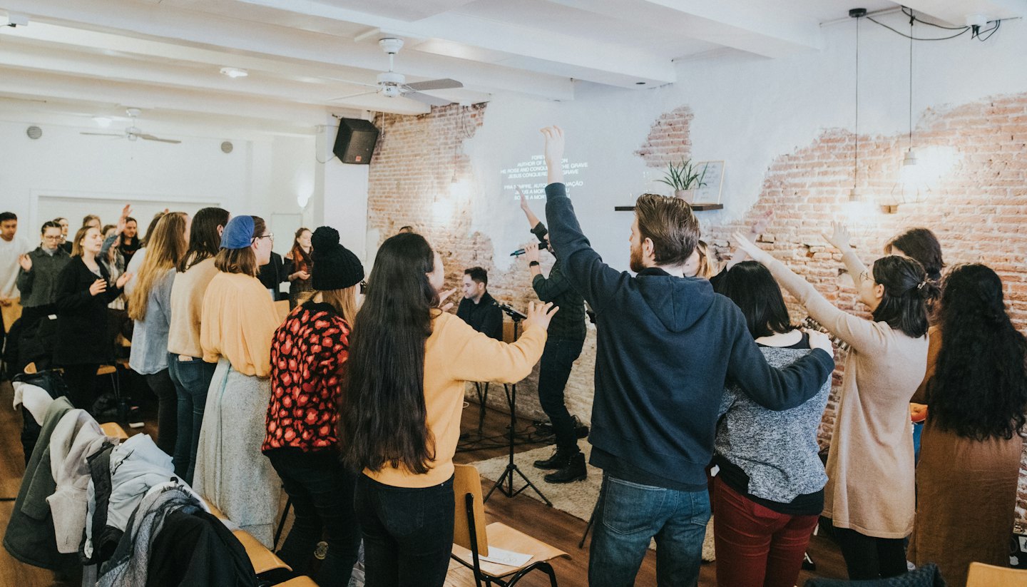 Young adults raise hands toward projected text on a brick wall.